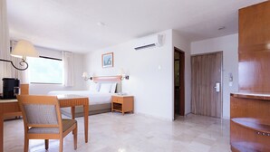 Ein Hotelzimmer mit Bett, Schreibtisch, Stuhl, Nachttisch, Klimaanlage und Holztür.