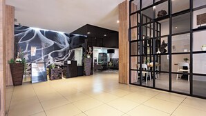 Eine geräumige Lobby im modernen Stil, mit einem großen Wandgemälde, einem Empfangsbereich und einer Sitzecke mit Stühlen und Tischen.