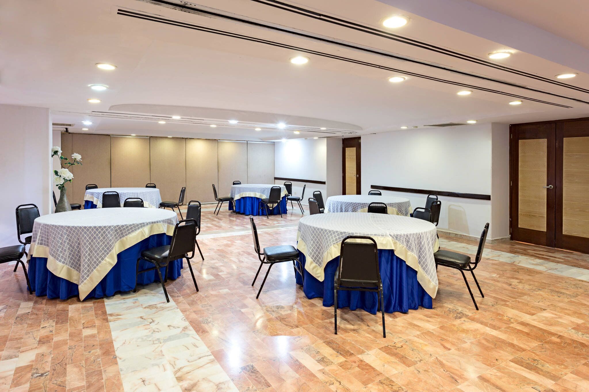Un salón de conferencias con mesas redondas, sillas y una pantalla para proyector.