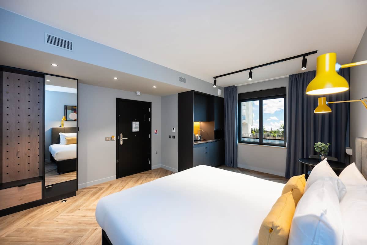 Une chambre d’hôtel moderne dotée d’un grand lit, d’un petit coin cuisine, d’un miroir et offrant une vue sur l’extérieur.