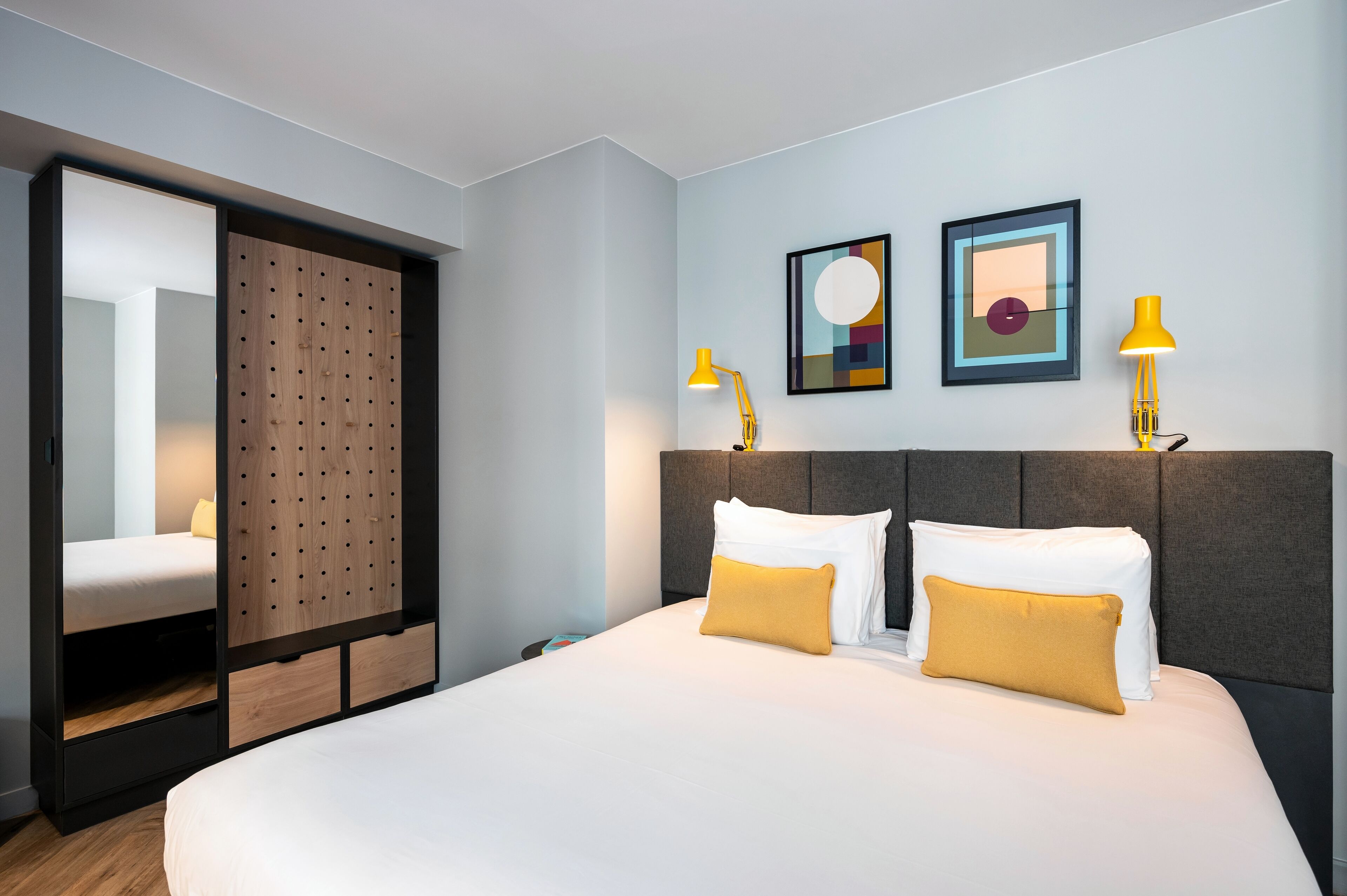 A modern hotel room with a large bed, two bedside lamps, and a wardrobe with a mirror.