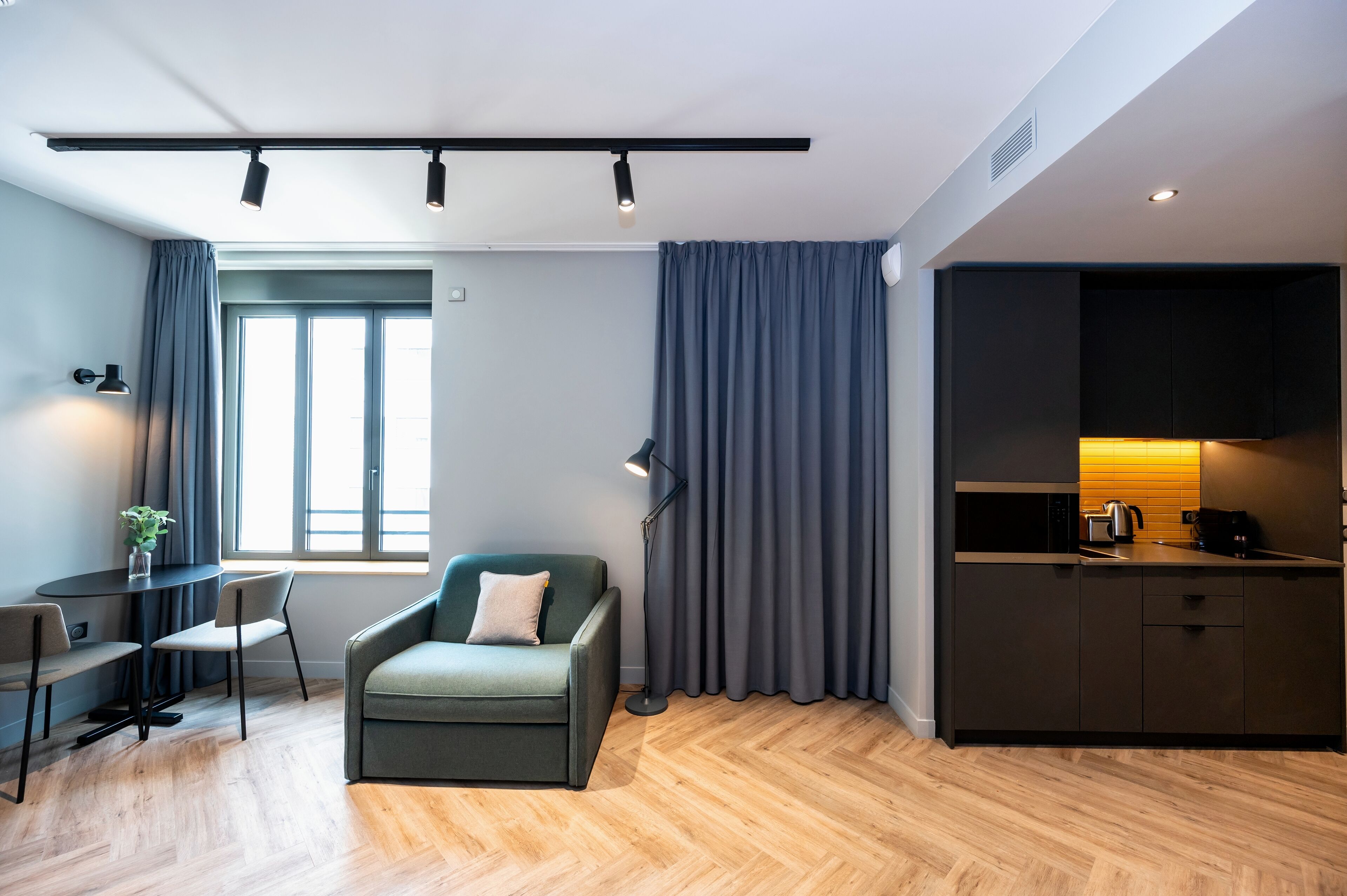 Una sala moderna con sofá, una mesa de comedor y sillas, un área de cocina con armarios y electrodomésticos, y un ventanal con cortinas.