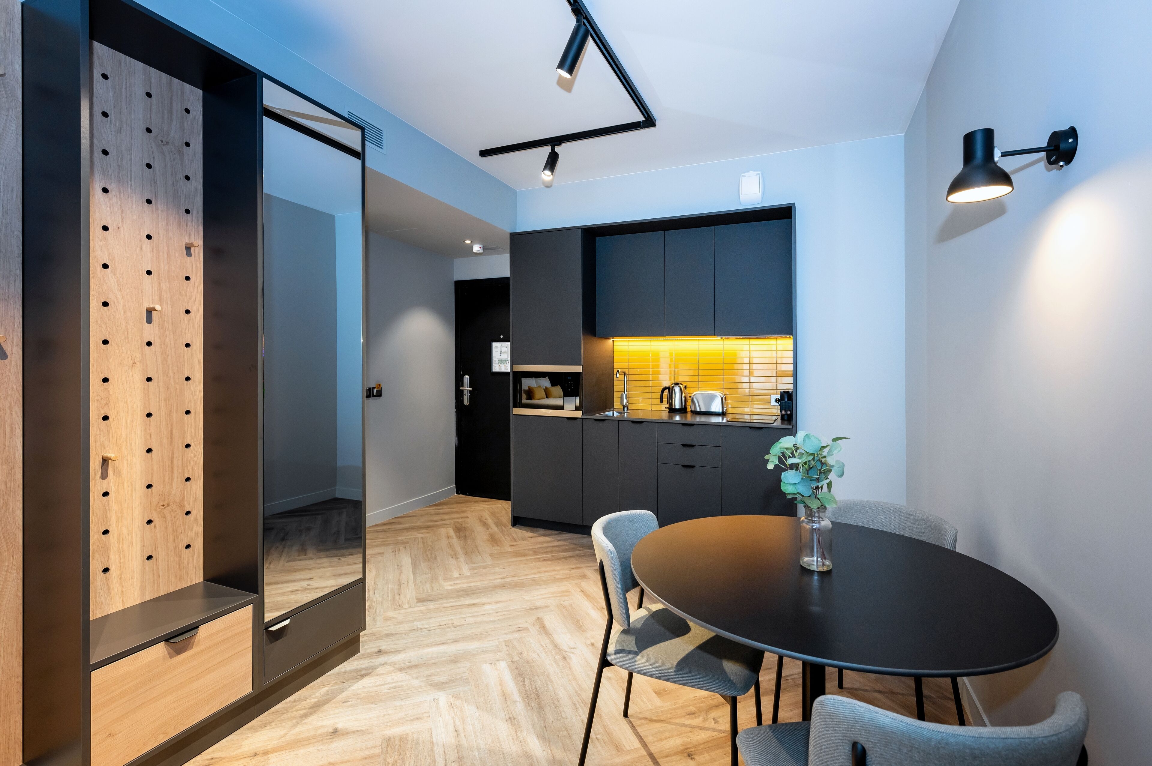 A modern kitchen with dark cabinetry, a wooden accent wall, and a round dining table with chairs.