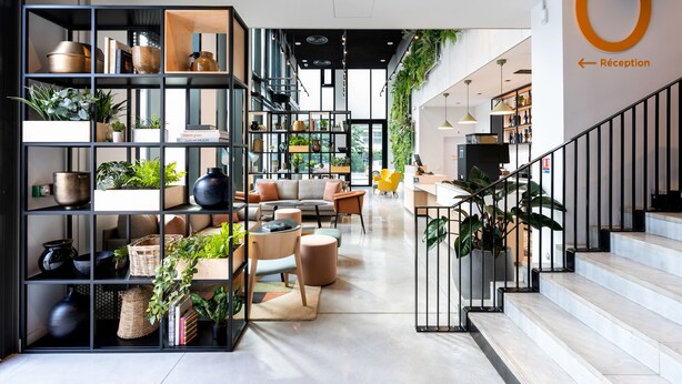 A modern hotel lobby with a reception desk, seating area, and a staircase.