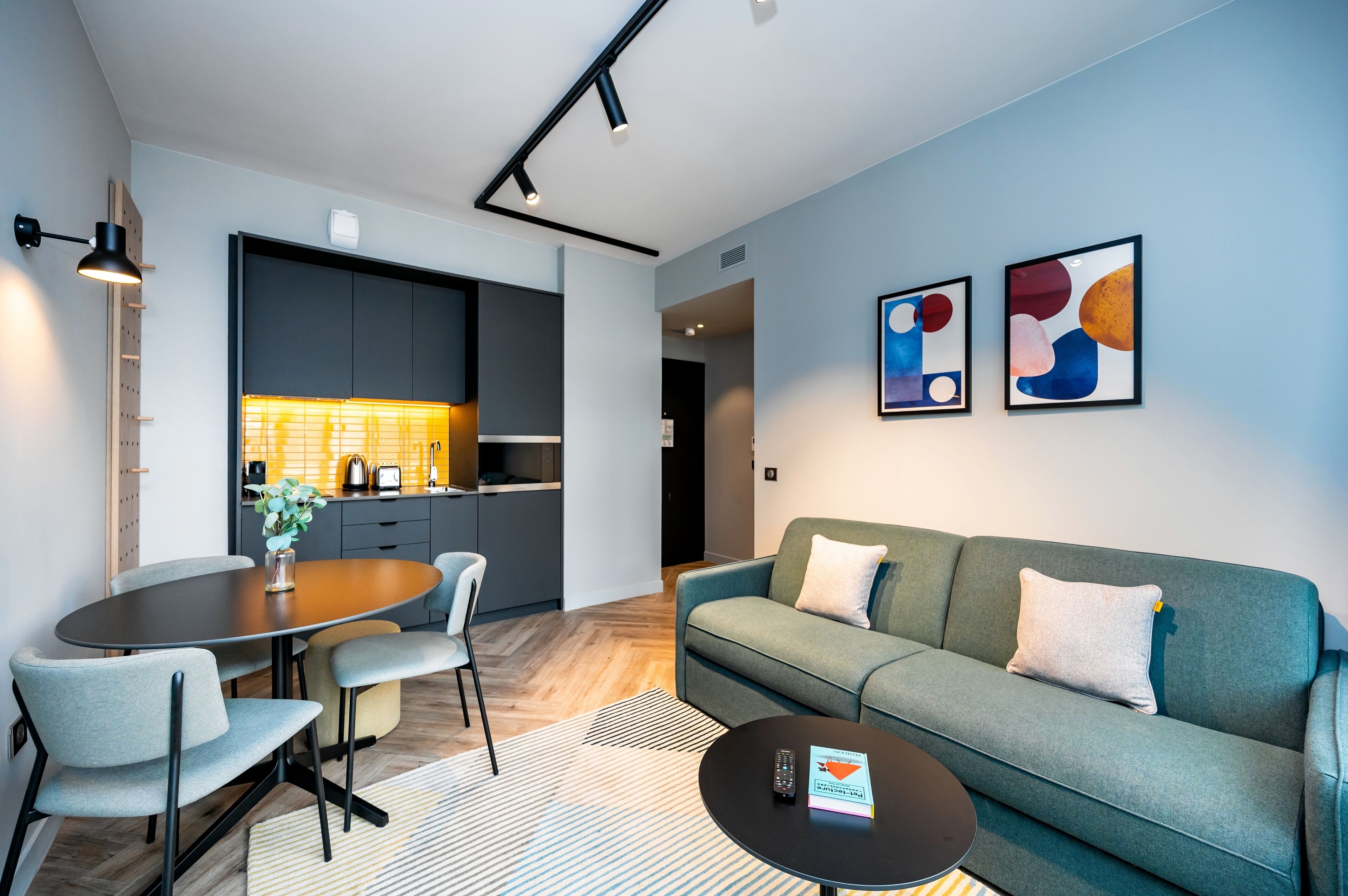 A modern living room with a sofa, a dining table with chairs, a coffee table, and abstract art on the wall.