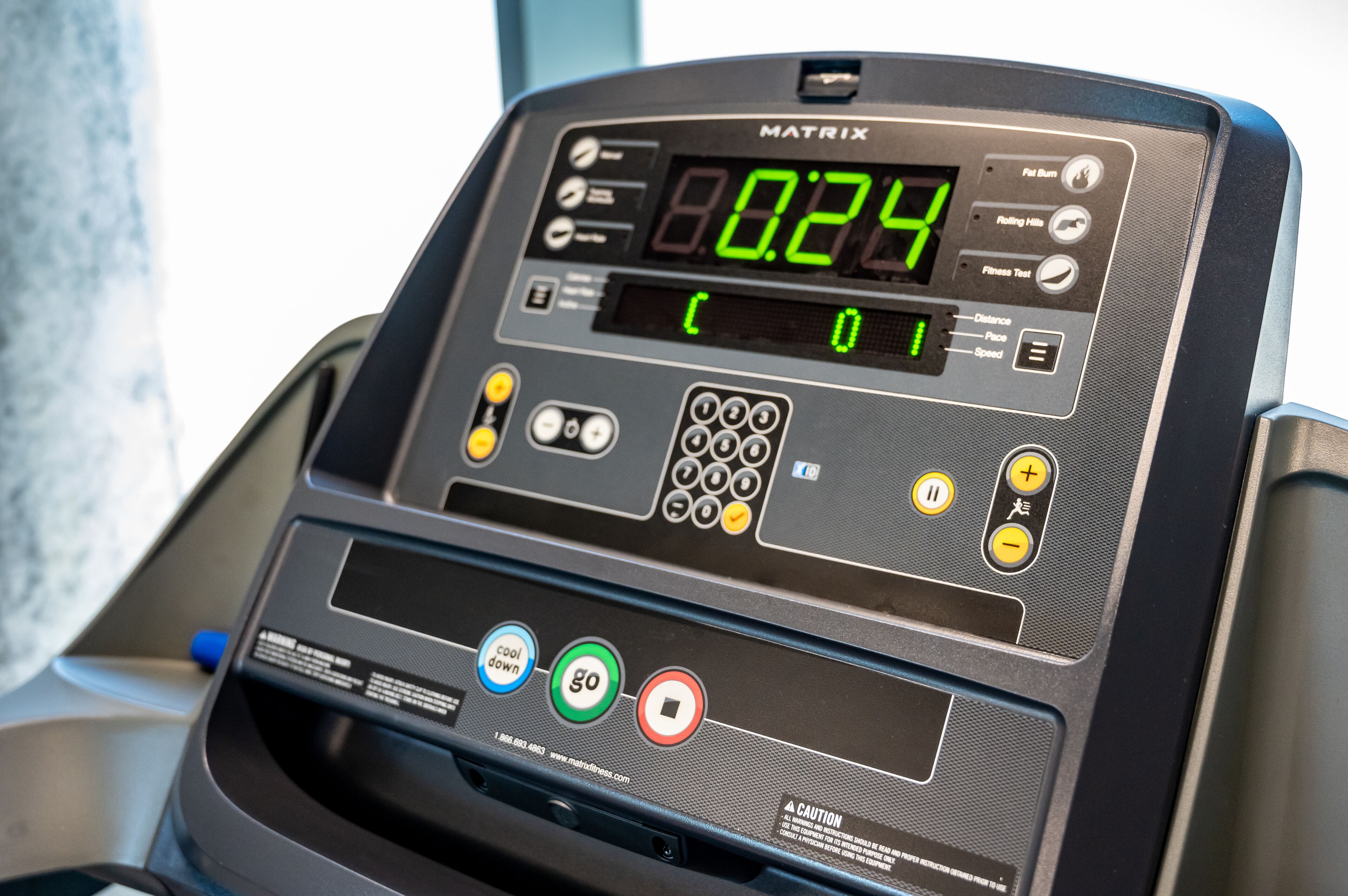 Una cinta de correr con pantalla digital, botones de control y una etiqueta de precaución.