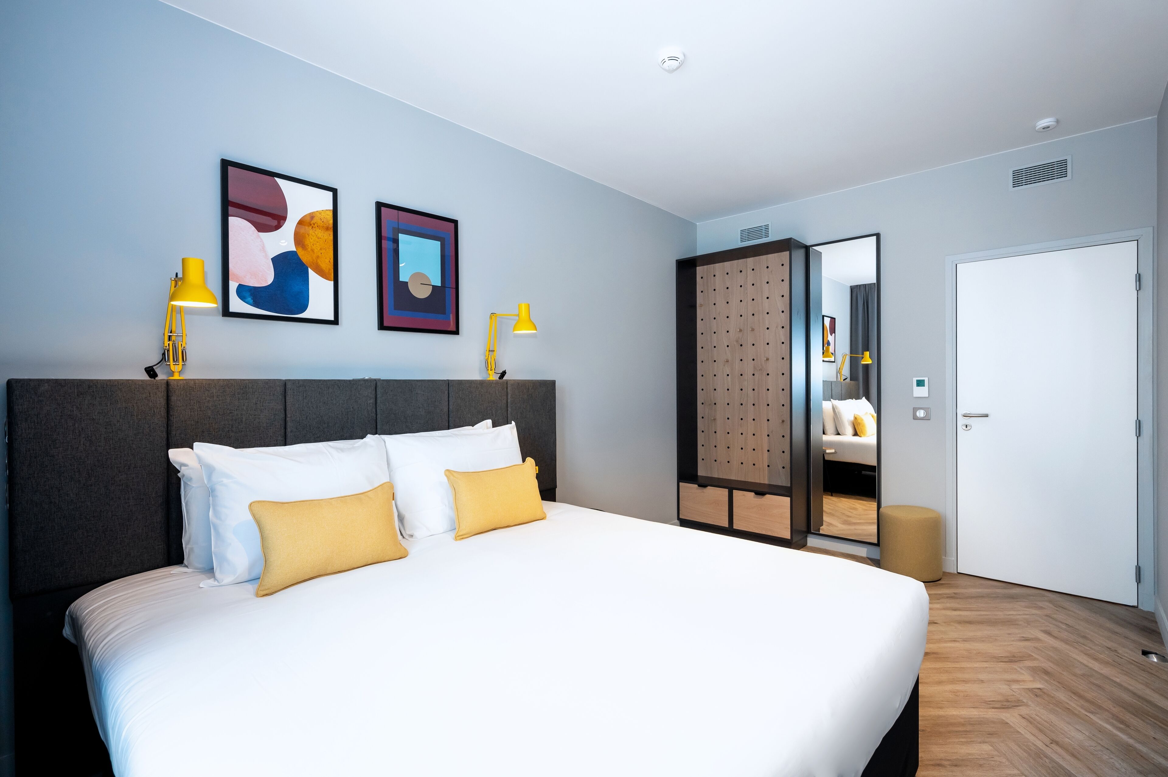 A modern hotel room with a large bed, two bedside lamps, and abstract art on the wall.