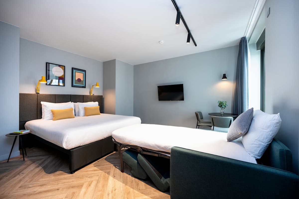 Une chambre d’hôtel moderne équipée de deux lits, d’un téléviseur à écran plat et d’une petite table avec une chaise.