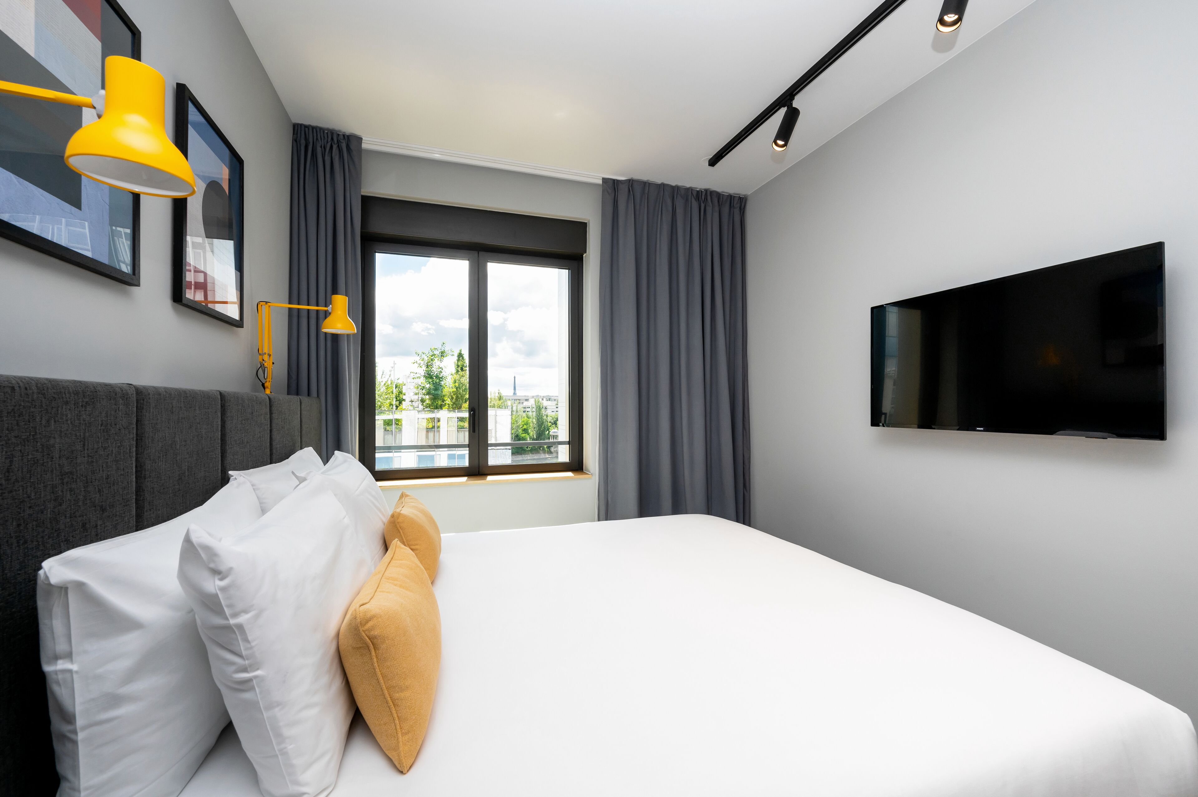 A modern hotel room with a large bed, a flat-screen TV, and a window with curtains.