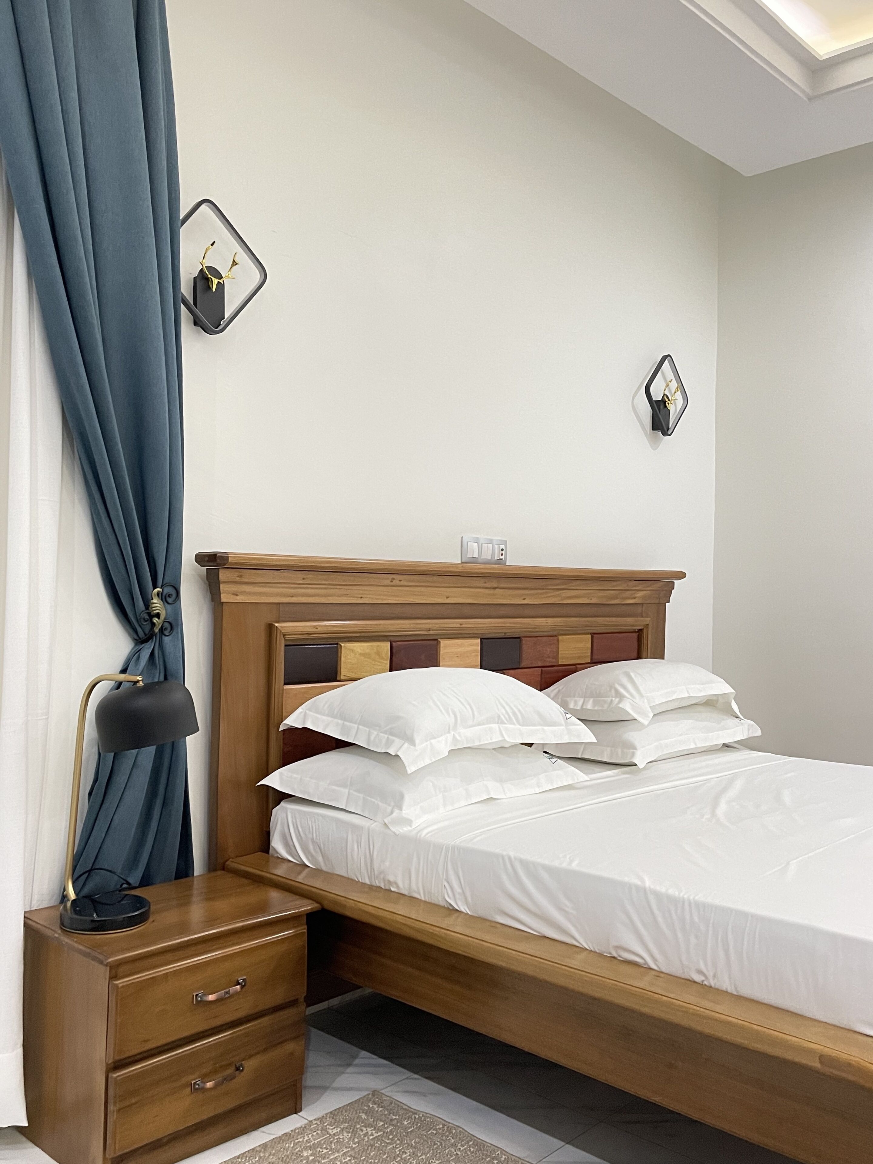 A neatly made bed with white linens, a wooden headboard, and a bedside table with drawers.