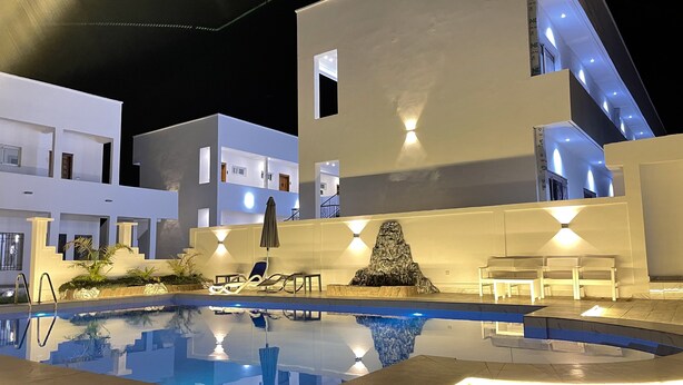 Uma área de piscina moderna com piscina transparente, escultura de rocha e mobiliário de exterior.
