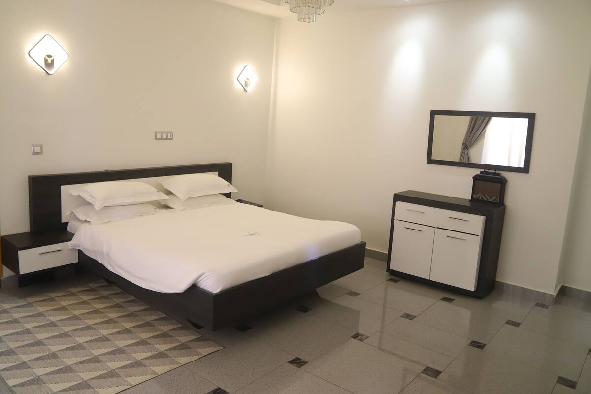 A modern bedroom with a bed, bedside tables, a dresser, and a mirror.