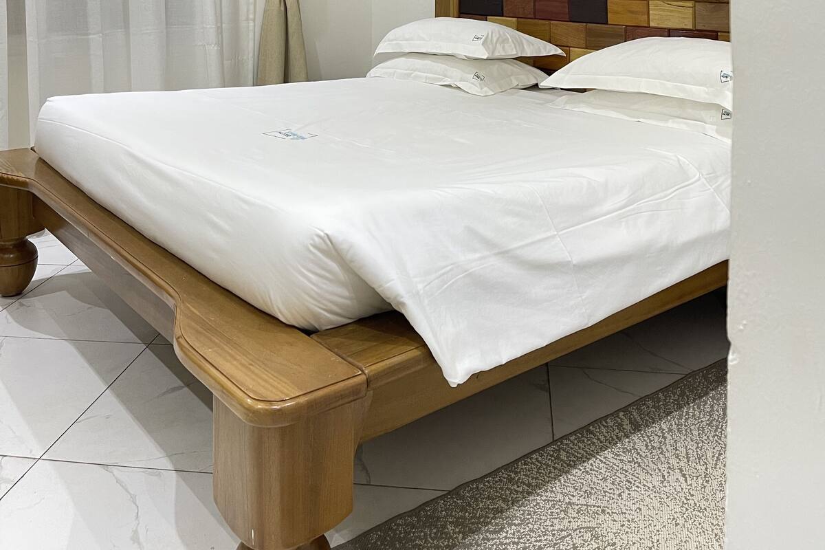 A neatly made bed with white linens, a wooden headboard, and an air conditioning unit mounted on the wall.