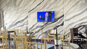 Uma sala de conferências com paredes de mármore, uma grande tela de televisão e cadeiras douradas dispostas em torno de uma mesa de vidro.