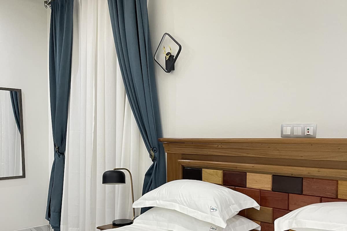 A hotel room with a bed, curtains, a bedside lamp, and a wall-mounted light fixture.