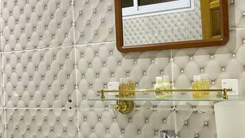A bathroom with a tufted wall, a glass shelf with toiletries, a white sink, and a mirror with a wooden frame.