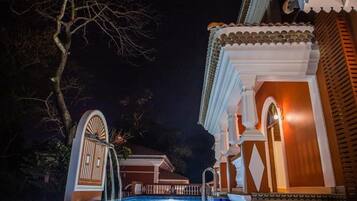Una piscina de estilo arquitectónico tradicional, una entrada con portones y una fachada de edificio bien iluminada.
