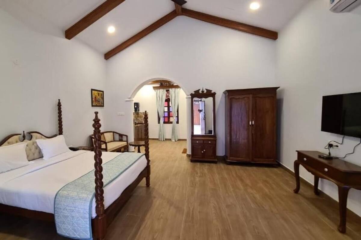Quarto com cama de madeira, guarda-roupa, escrivaninha e televisão.