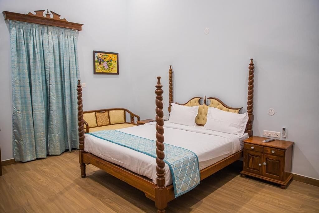 A four-poster bed with a wooden frame, a nightstand with a drawer, and a window with light blue curtains.