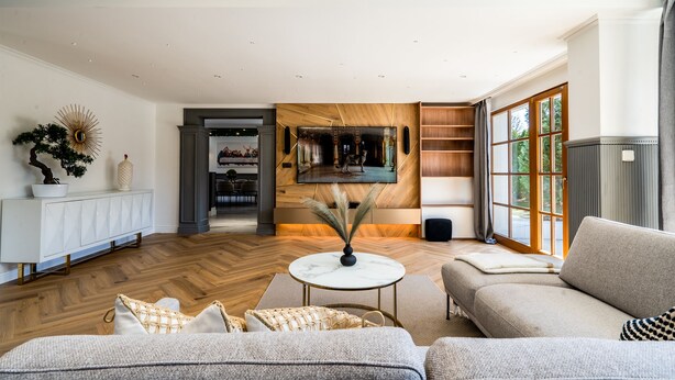 A spacious living room with a large sofa, a coffee table, and a TV. There is a wooden floor, a white cabinet, and a large window. - Serenity Prague Villa with garden jacuzzi (Pruhonice)