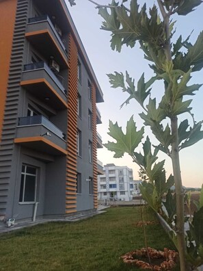 A modern multi-story building with balconies, a grassy area, and a tree. - Hilar Otel (Ergani)