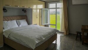 Et soveværelse med seng, skab, et vindue med udsigt over det åbne landskab og en aircondition.