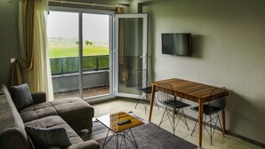 En stue med sofa, sofabord, tv og en balkon med udsigt over landskabet.