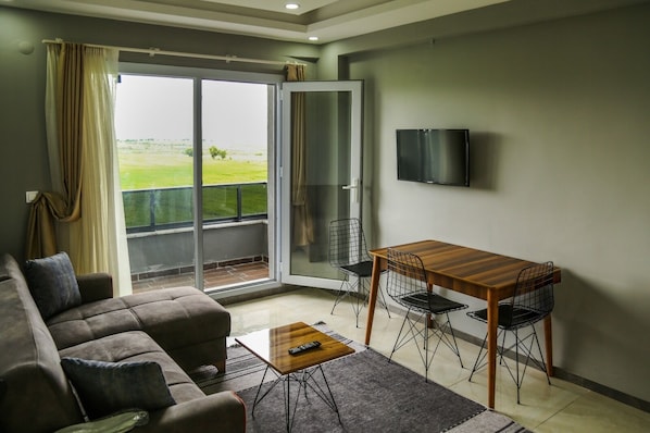 Una sala de estar con un sofá, una mesa de centro, un televisor y un balcón con vistas al campo.