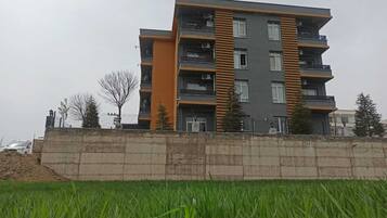 Een meerlaags woongebouw met balkons, een betonnen steunmuur en een grasveld op de voorgrond.