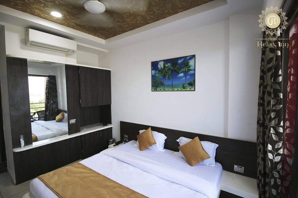 A hotel room with a bed, a large mirror, a painting of a beach scene, and a window with curtains.