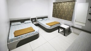 Habitación de hotel con dos camas, una mesita, un ventilador de techo y una ventana con cortina.
