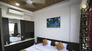 Habitación de hotel con cama, un espejo grande, un cuadro de palmeras y una ventana con cortinas.