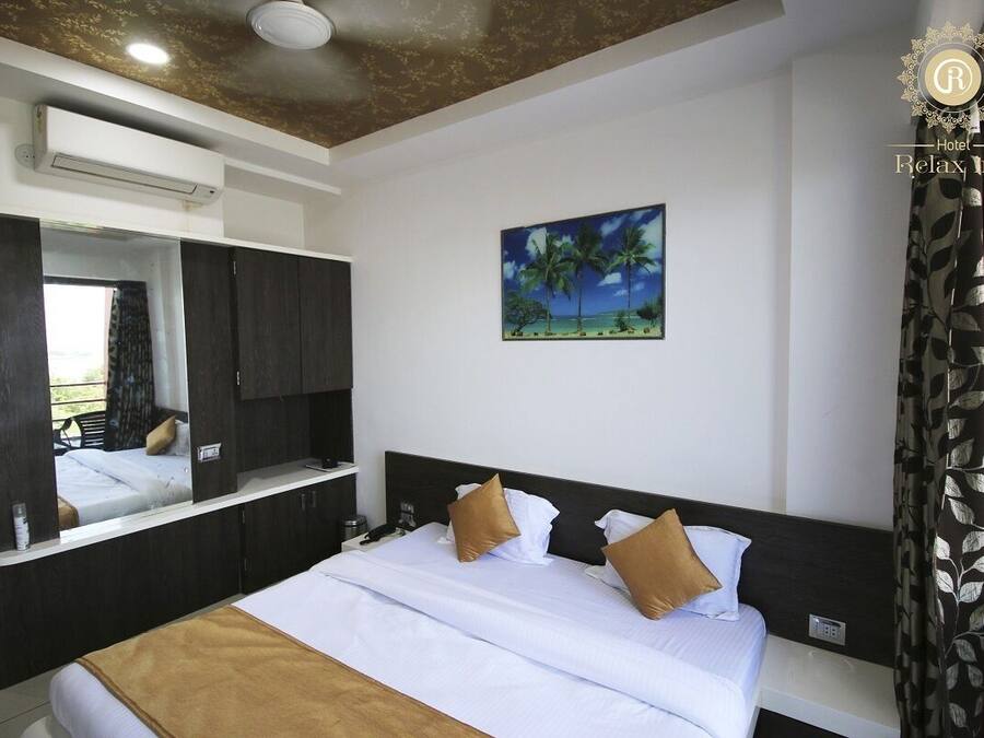 A hotel room with a bed, a large mirror, a painting of palm trees, and a window with curtains.