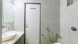 Un baño con lavamanos blanco, un espejo, ducha con cabezal de ducha manual y un inodoro.
