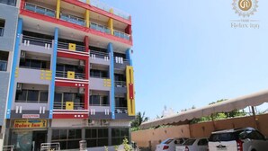 Un hotel de varios pisos con recepción en la planta baja, balcones en cada nivel y un estacionamiento con varios automóviles.