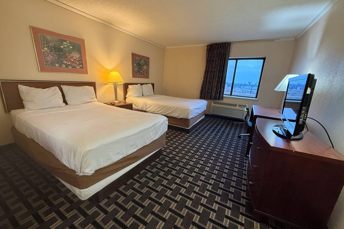 A hotel room with two beds, a desk, a computer, and a window with a view.