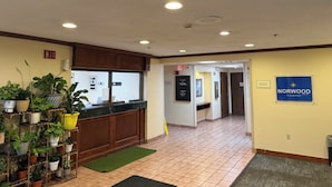 A hotel lobby with a reception desk, potted plants, a sign for Norwood by Blisspoint, and a tiled floor. - Norwood Inn & Suites by BlissPoint Post Rd Indianapolis (Indianapolis)