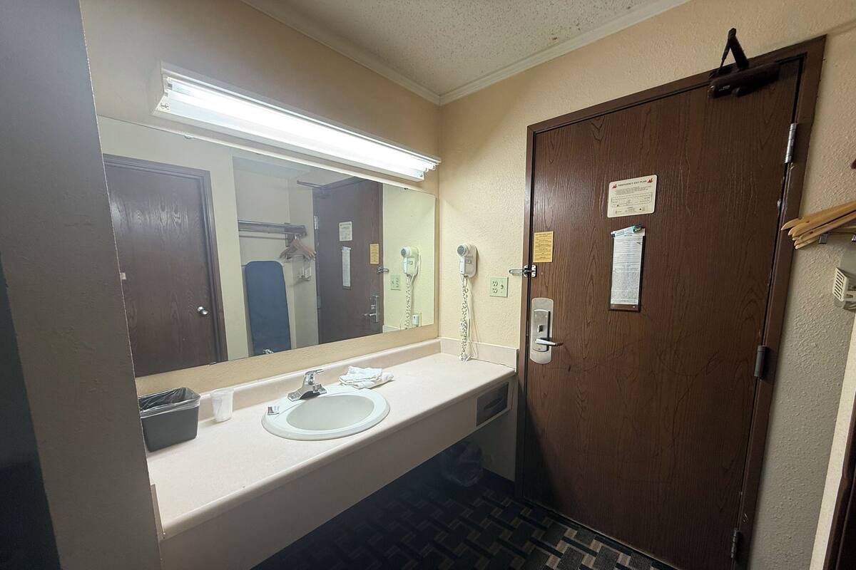 A hotel bathroom with a sink, mirror, and a door with a paper notice.