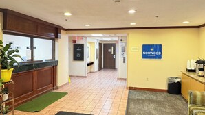 A hotel lobby with a reception desk, a welcome sign, a trash bin, and a coffee station. - Norwood Inn & Suites by BlissPoint Post Rd Indianapolis (Indianapolis)