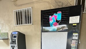 An ATM and a vending machine with various drink options. - American Inn (Perris)
