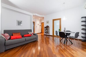 Un salon moderne avec un canapé gris, des coussins rouges, une table à manger avec des chaises et un plancher en bois.