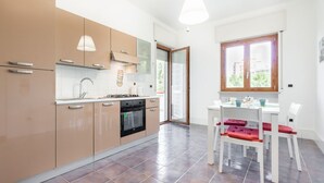 A modern kitchen with beige cabinets, a stove, and a dining area with white chairs and a table. - GuestHost - Roomy and tastefully furnished apartment, ideal for families as it accommodates up to 6 people having 2 bedrooms, 2 bathrooms, a balcony and an equipped terrace. The flat is located in a residential context with concierge and internal garden, (Bari)