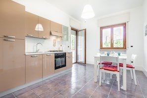 A modern kitchen with beige cabinets, a stove, and a dining area with white chairs and a table.