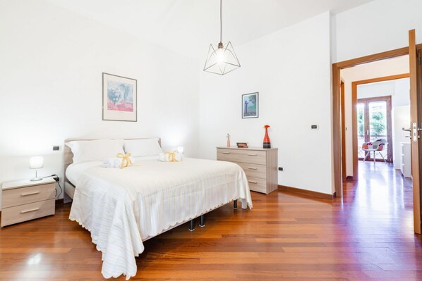 Une chambre à coucher comprenant un lit, des tables de chevet, une commode et un luminaire suspendu.