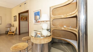 Un intérieur moderne avec une table ronde en verre, un tabouret de bar, une lampe et une étagère fixée au mur.