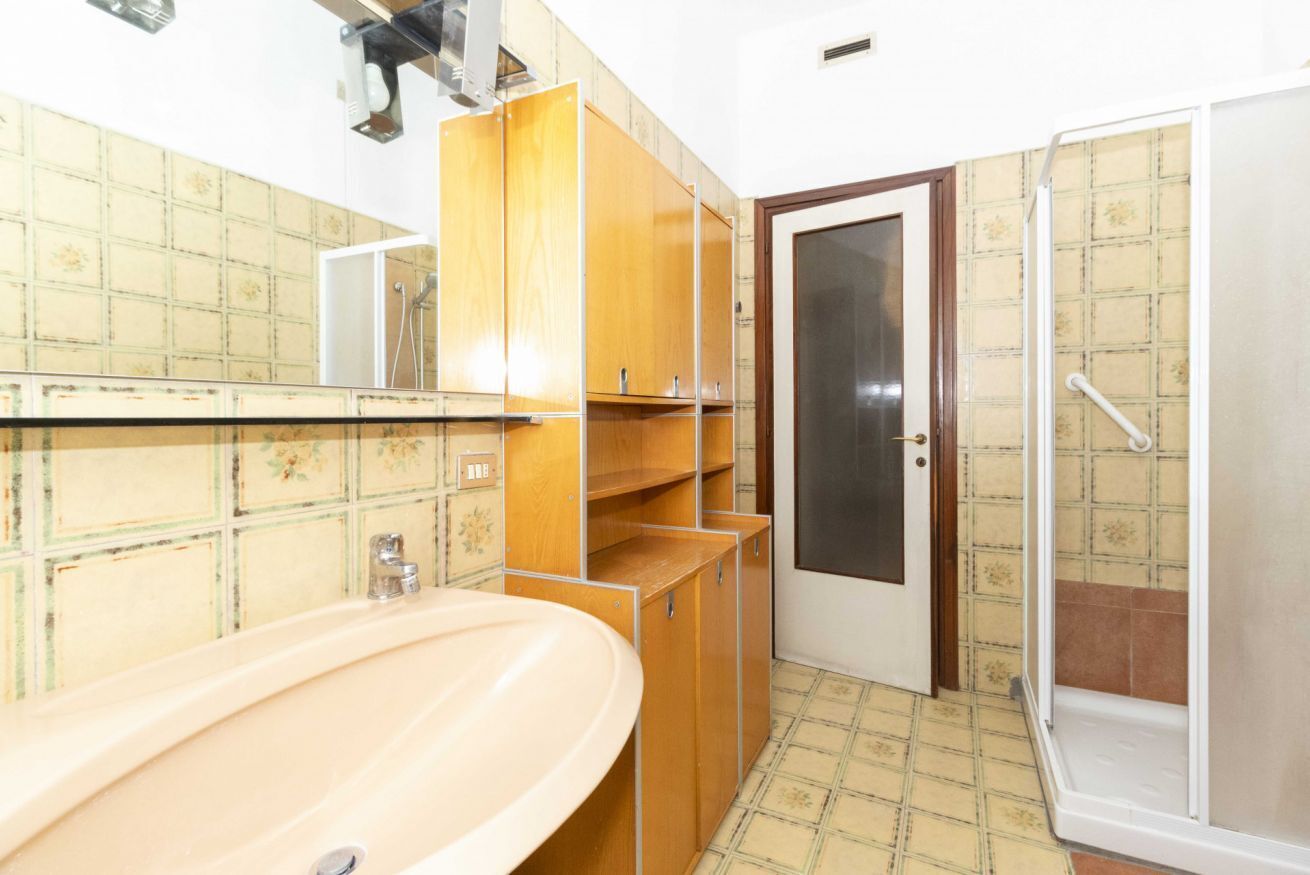 A bathroom with a sink, wooden cabinets, a shower, and a door with a frosted glass panel.