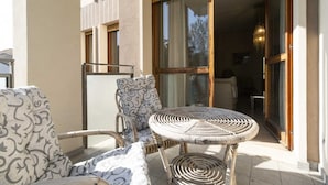 Un balcon doté de meubles en osier, une porte vitrée donnant sur un espace intérieur et un sol carrelé.