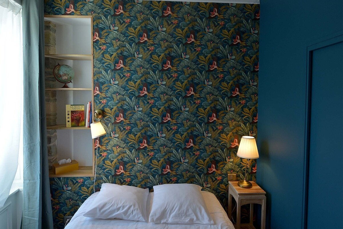 A bedroom with a bed, two bedside lamps, a bookshelf, and a patterned wallpaper.