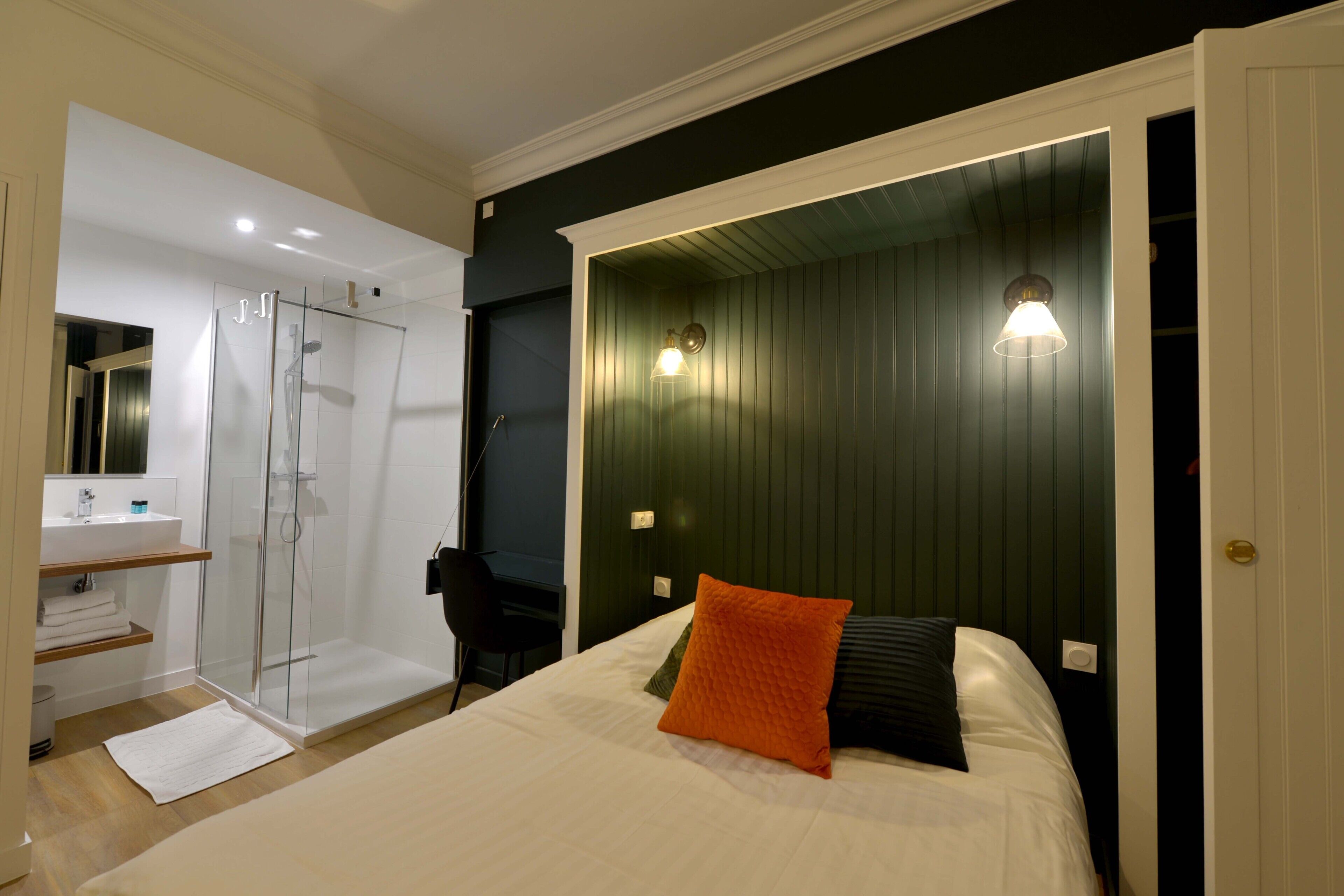 A bedroom with a bed, a nightstand, a bedside table, a mirror, a window, and a door.