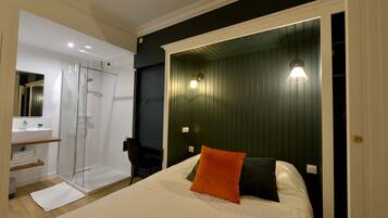 A bedroom with a bed, a nightstand, a bedside table, a mirror, a window, and a door.